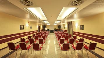 A hotel conference room with rows of red chairs and a stage at the front.