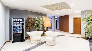A lobby with a vending machine, two white armchairs, a potted plant, and a wooden door. - Airport Hotel (Bagnatica)