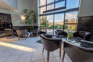 Un área de estar interior moderna con sillones de cuero y una mesa de vidrio, ventanas amplias que ofrecen vistas al exterior y plantas en macetas que aportan verdor.