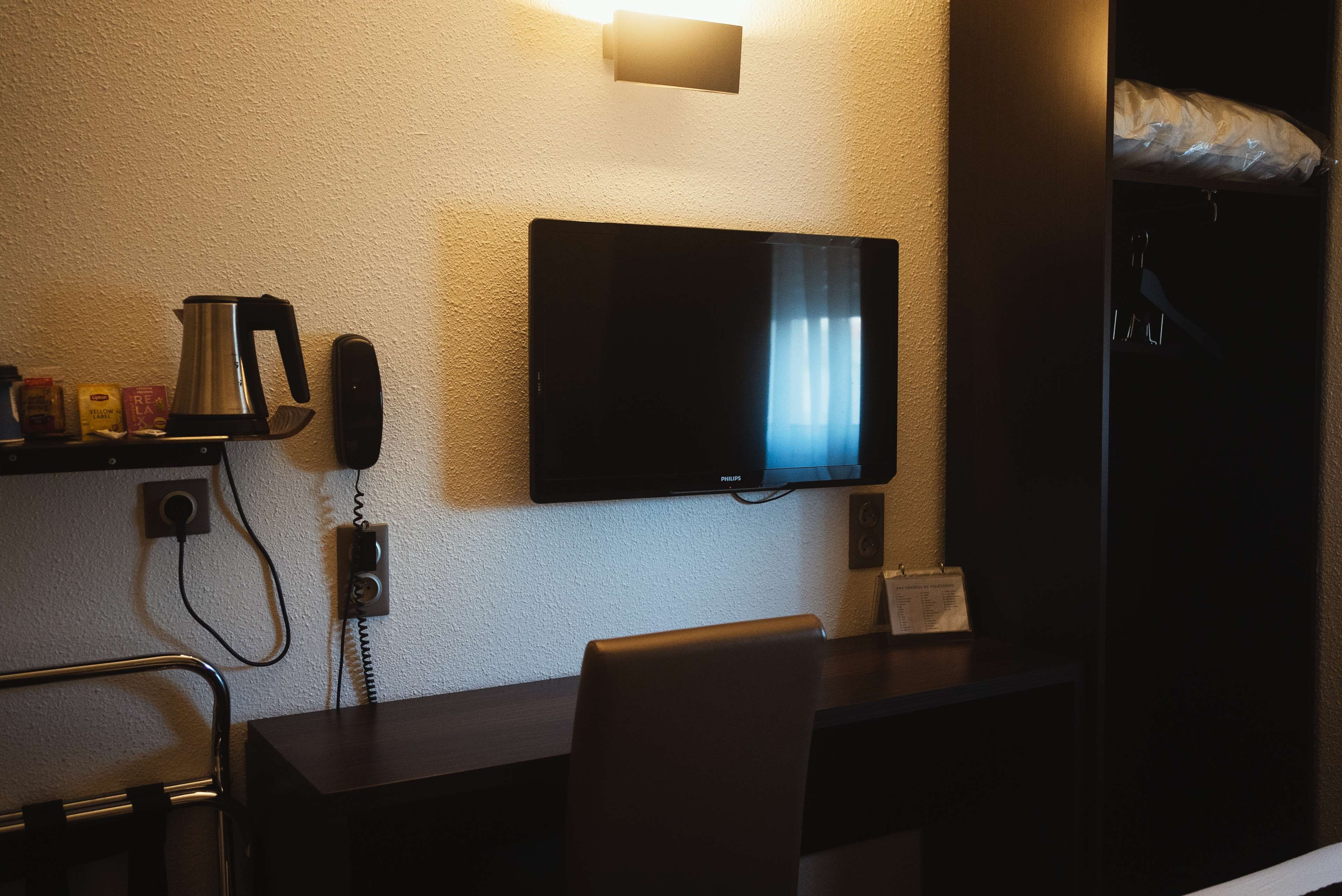 A hotel room with a flat-screen TV mounted on the wall, a coffee maker, a telephone, and a chair.