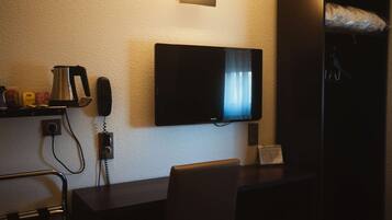 Ein Hotelzimmer mit Wandfernseher, einer Kaffeemaschine, einem Telefon und einem Sessel.