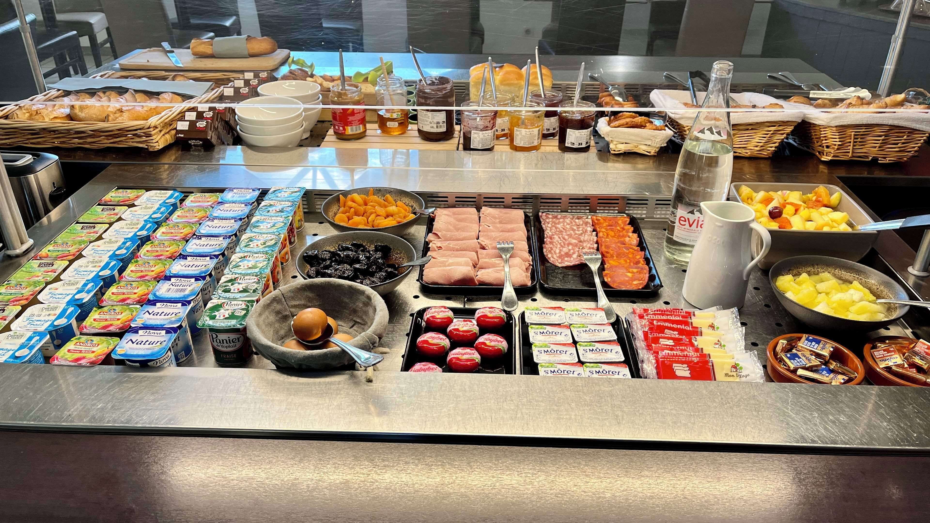 Un bufé con diferentes opciones de comida, incluyendo pan, bollería, quesos y salsas.