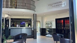 Un hall d’hôtel comprenant un comptoir d’accueil, un espace salon et une vitrine en verre contenant des bouteilles.