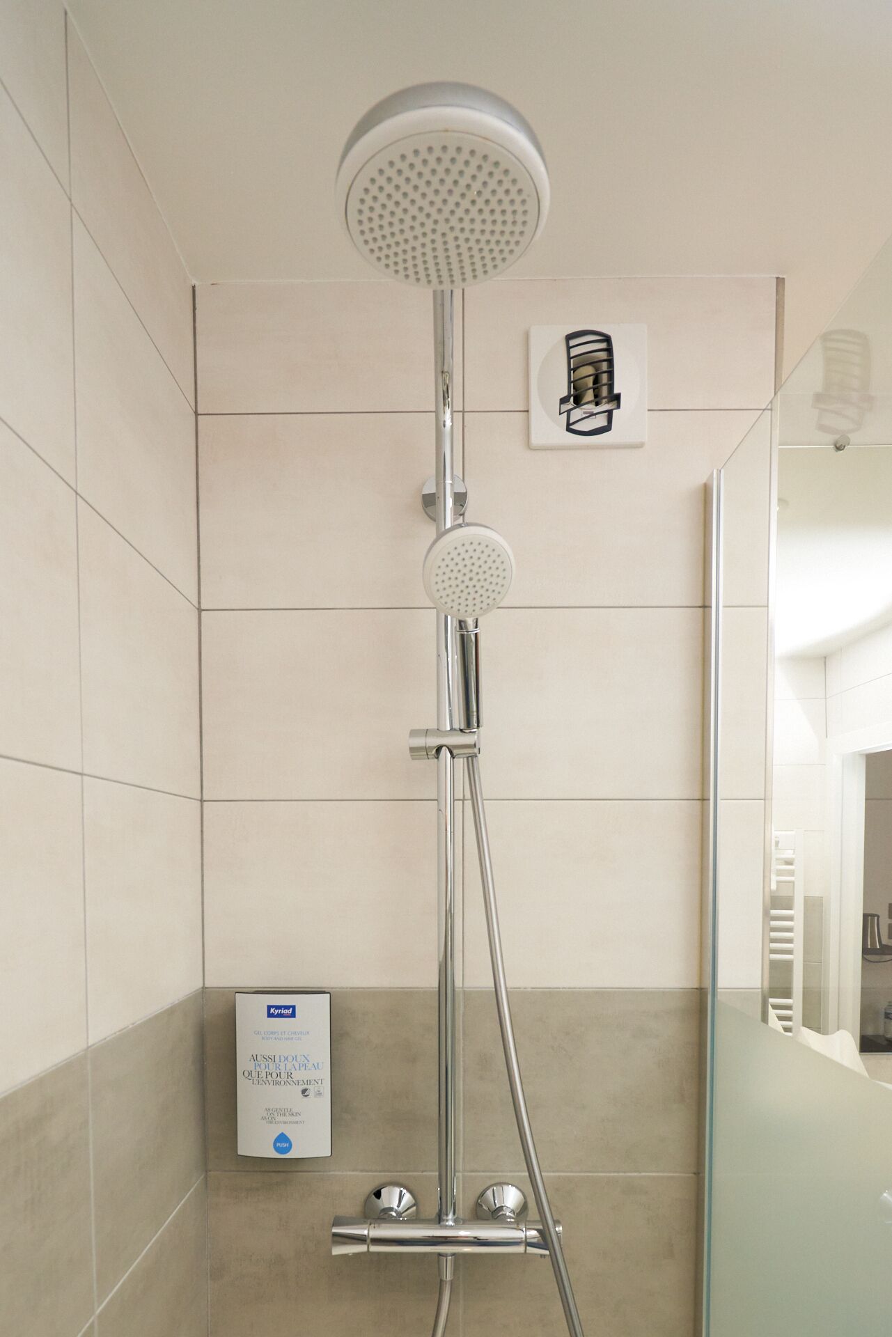 Une douche moderne dotée d’un pommeau rond, d’un pommeau de douche à main et d’un panneau de commande mural.