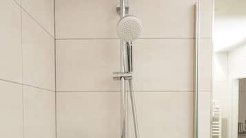 Une douche moderne dotée d’un pommeau rond, d’un pommeau de douche à main et d’un panneau de commande mural.