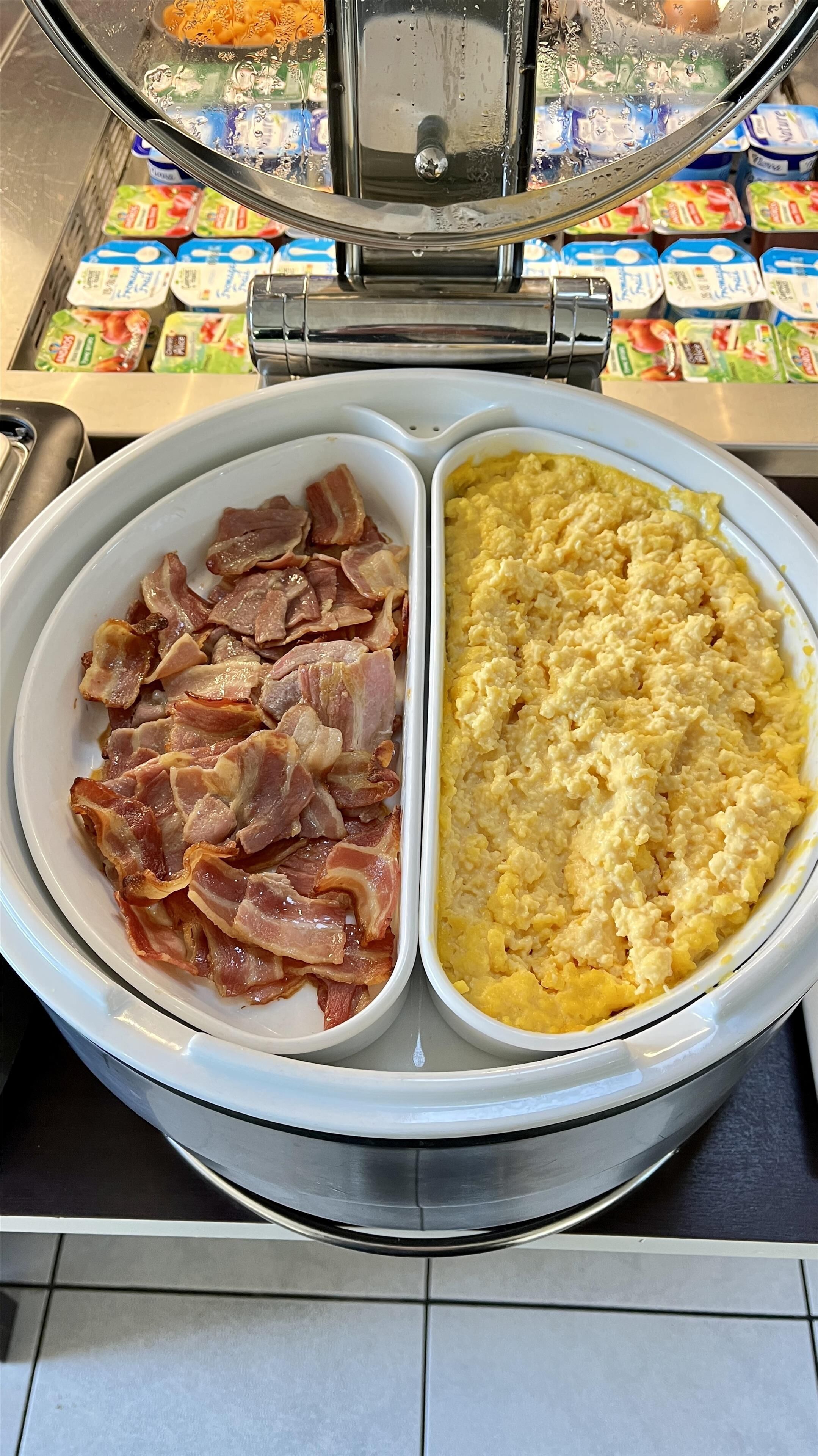 Un buffet de petit-déjeuner proposant deux plats distincts : un avec du bacon et l’autre avec des œufs brouillés.