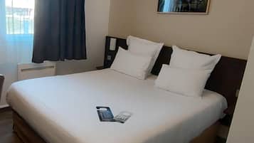 A hotel room with a large bed, a nightstand, a wall-mounted phone, and a window with curtains.