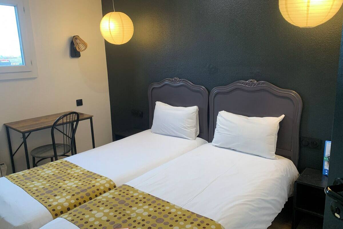 Un lit double avec une literie blanche, une petite table avec une chaise et deux lampes fixées au mur.