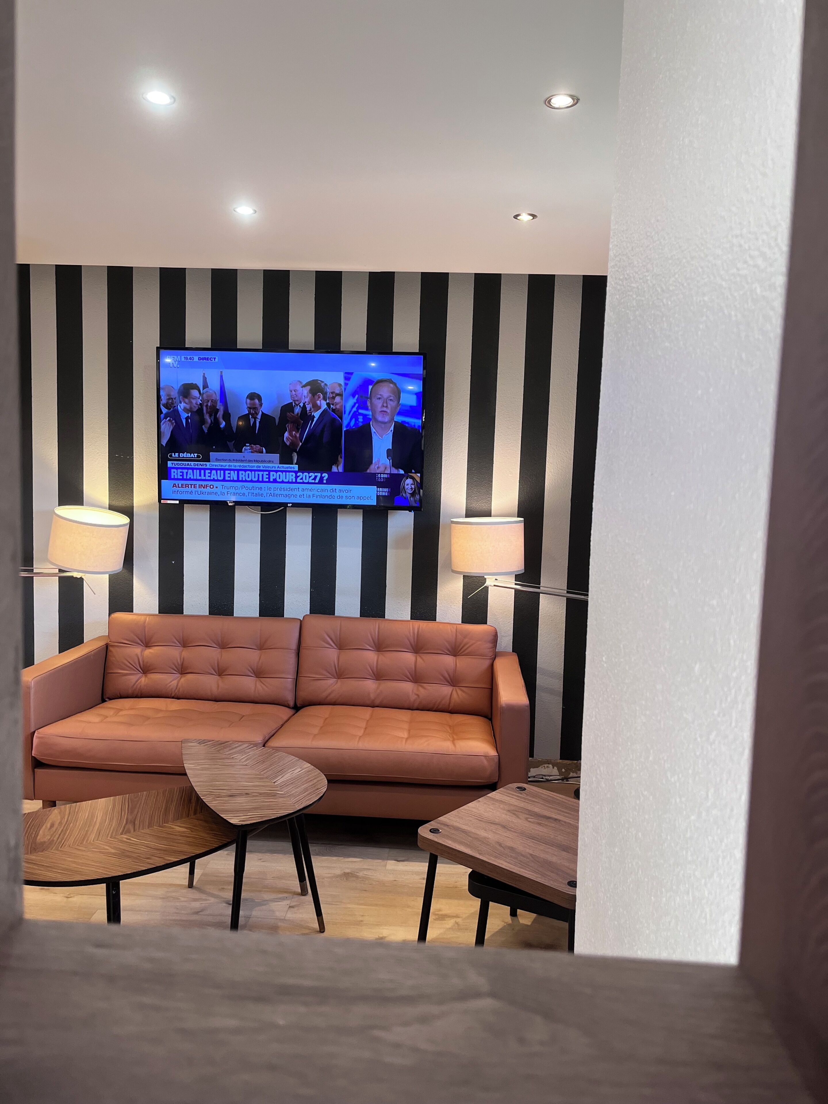 A living room with a sofa, two side tables, a television mounted on a striped wall, and two floor lamps.