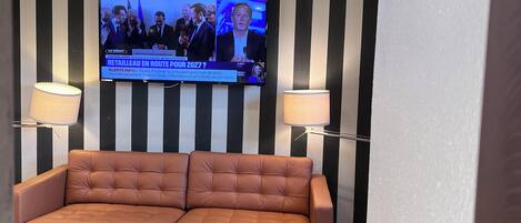 A living room with a sofa, two side tables, a television mounted on a striped wall, and two floor lamps.