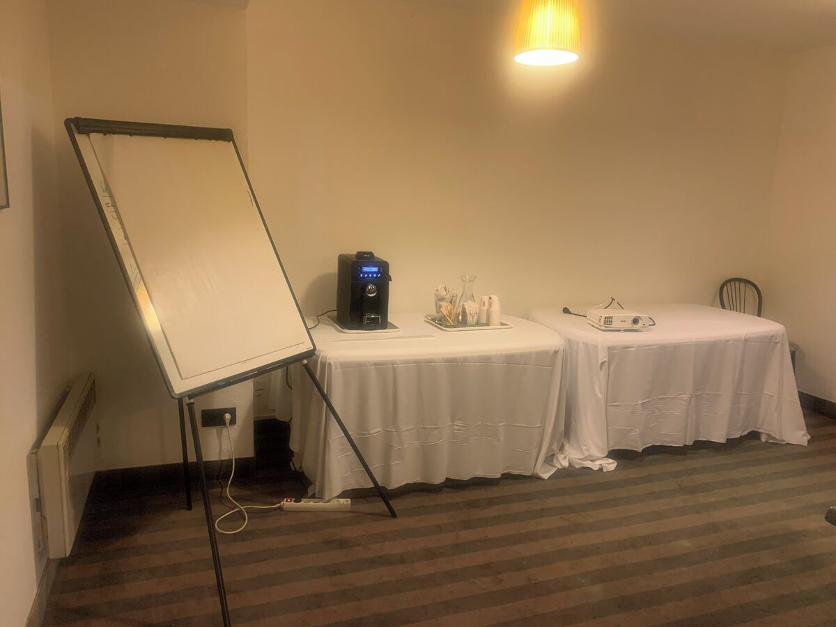 Una sala de conferencias con una pizarra, proyector y mesa cubierta con un mantel blanco.
