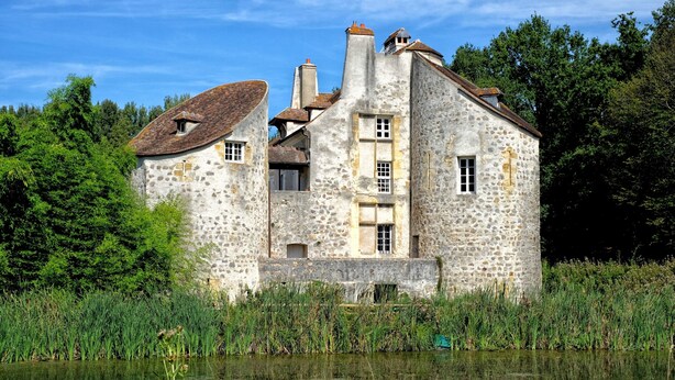 A stone building with multiple windows and a pond in front.