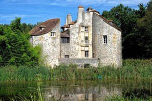 Ein Steinhaus mit vielen Fenstern und einem Teich davor.