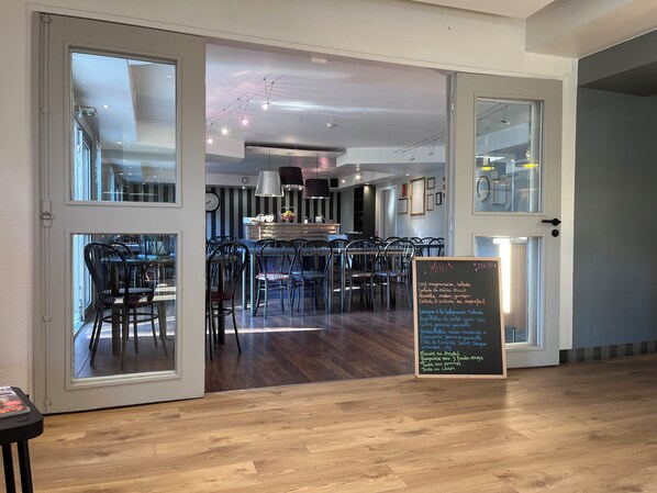 An interior view of a restaurant with a chalkboard menu, wooden flooring, and modern furnishings. - Brit Hotel Baillet en France (Baillet-en-France)