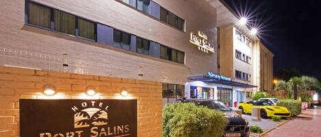 A hotel named "Port Salins" with a signboard, a restaurant named "Notray Restaurant" across the street, and several luxury cars parked in front.