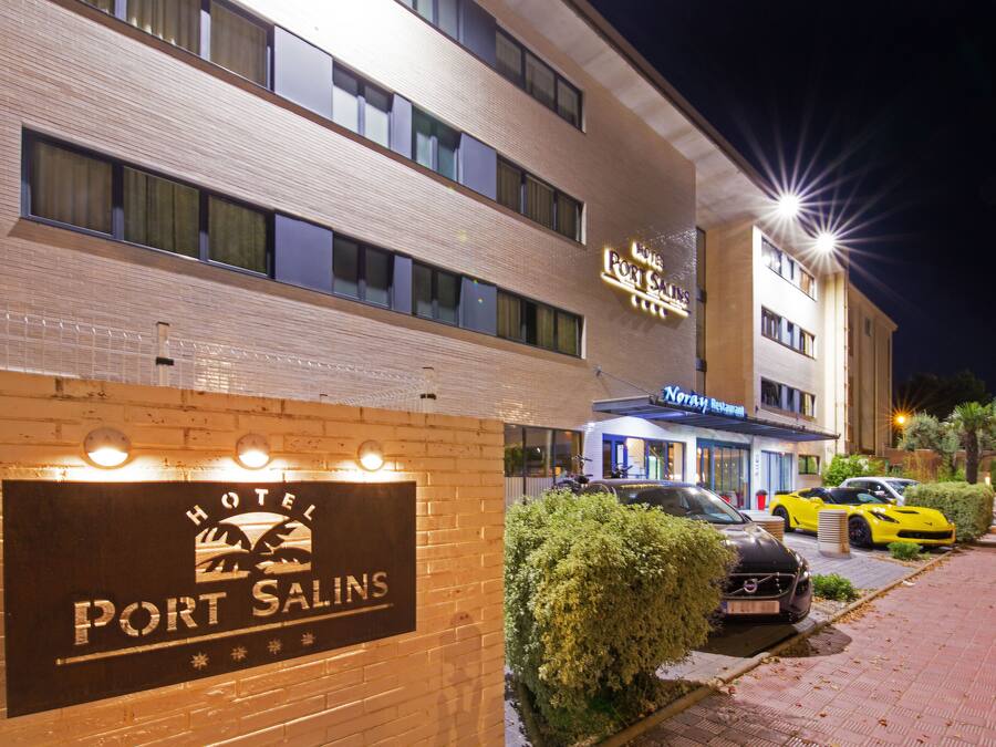 Ein Hotel namens "Port Salins" mit einer Schautafel, ein Restaurant namens "Notray Restaurant" gegenüber und mehrere luxuriöse Autos vor der Fassade.