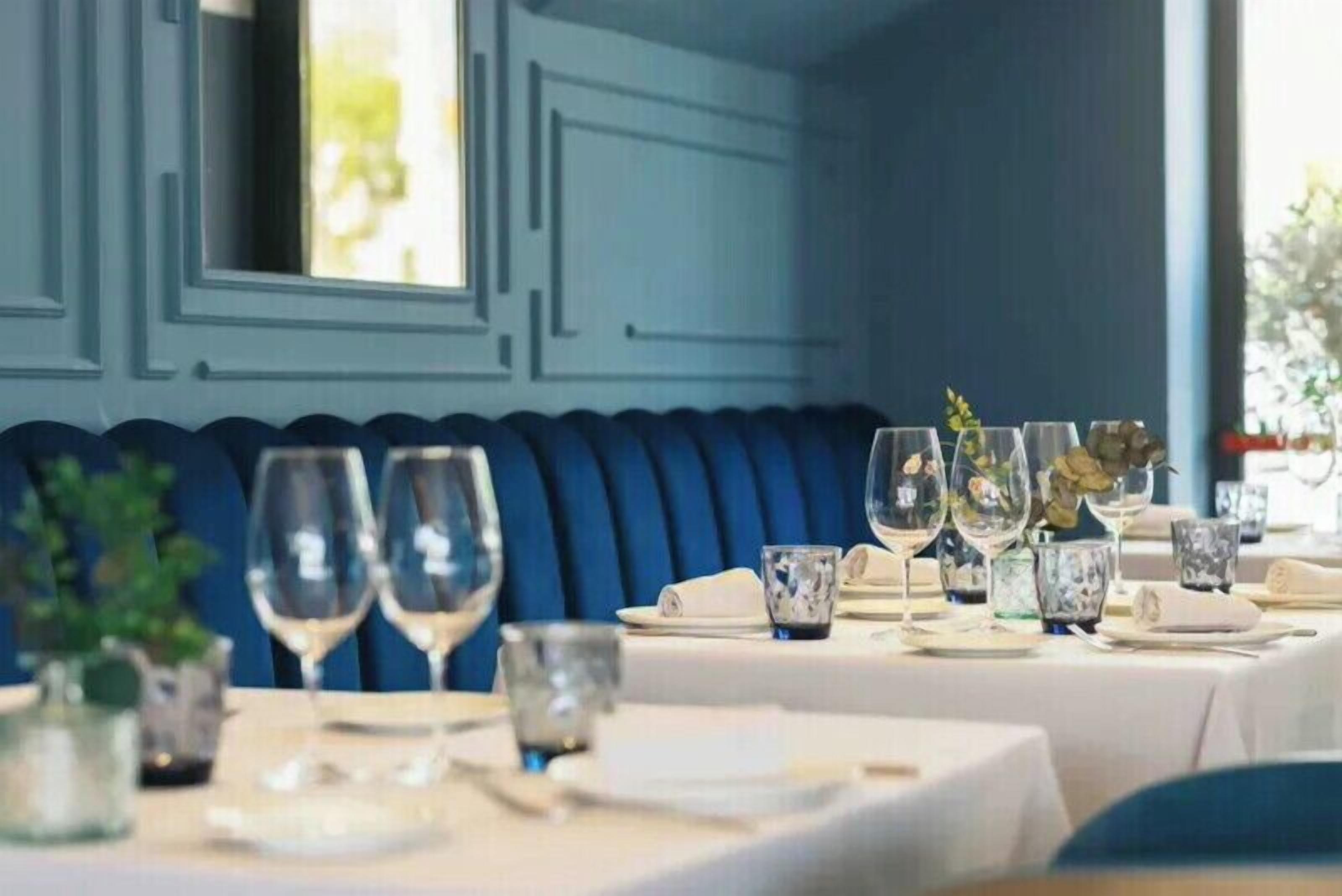 A dining area with tables set for a meal, featuring blue upholstered seating and clear glassware.