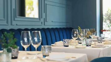 Comedor con mesas dispuestas para una comida, con asientos tapizados en azul y cubiertos de vidrio transparente.