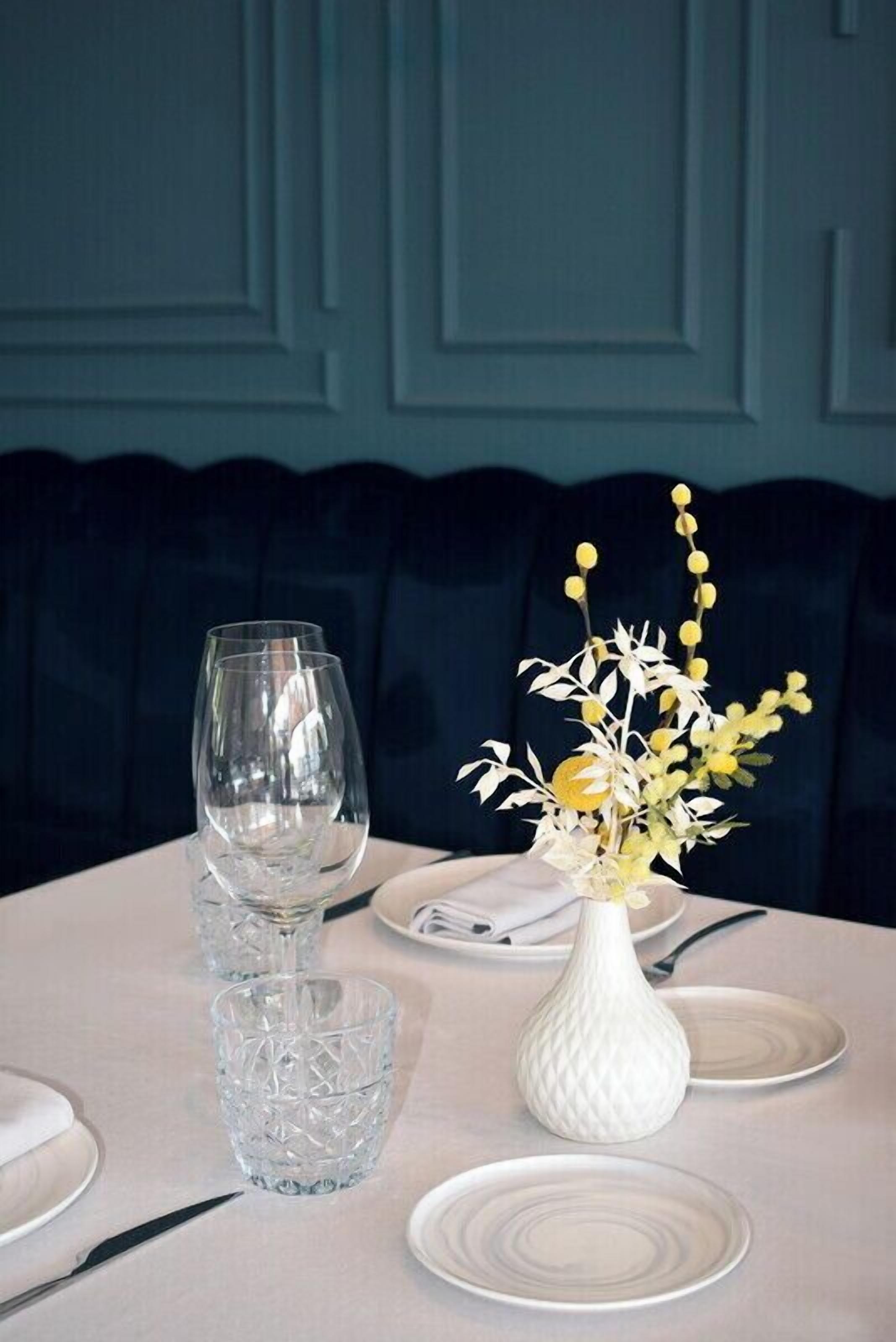 Een eettafel gedekt met een witte vaas, twee wijnglazen en een klein glas.