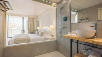 A modern hotel room with a large bed, a walk-in shower, and a bathroom with a large sink and mirror.