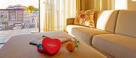 Un salon moderne avec un canapé, une boîte rouge en forme de cœur, une rose et un ordinateur portable.