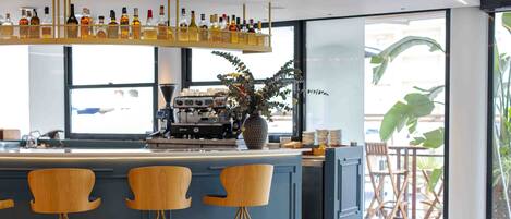 Zona de bar moderna con mostrador, tres taburetes de madera y una variedad de botellas en un estante.