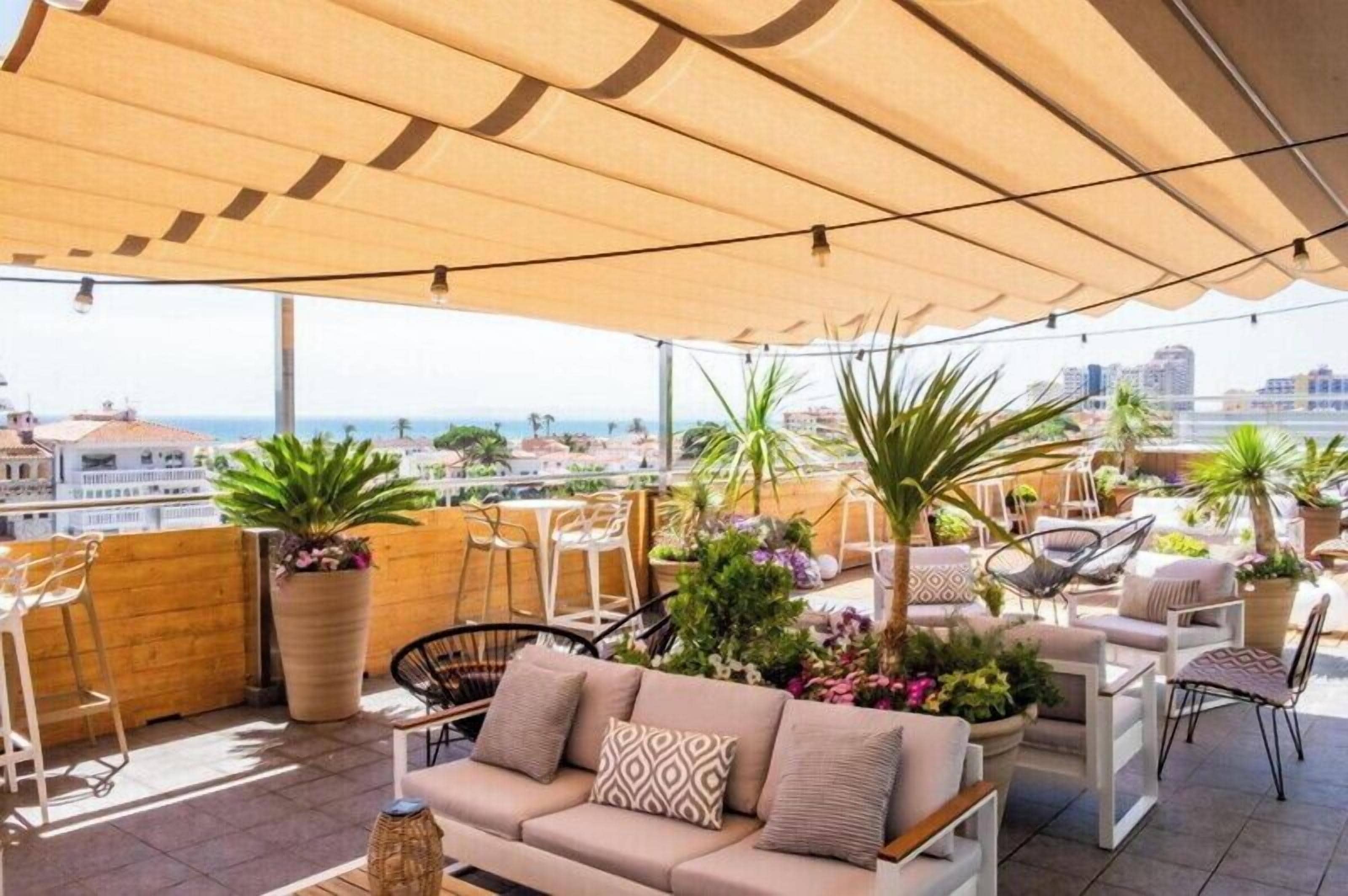 A rooftop terrace with outdoor seating, potted plants, and a view of the city.