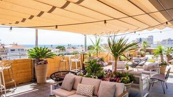 A rooftop terrace with outdoor seating, potted plants, and a view of the city.