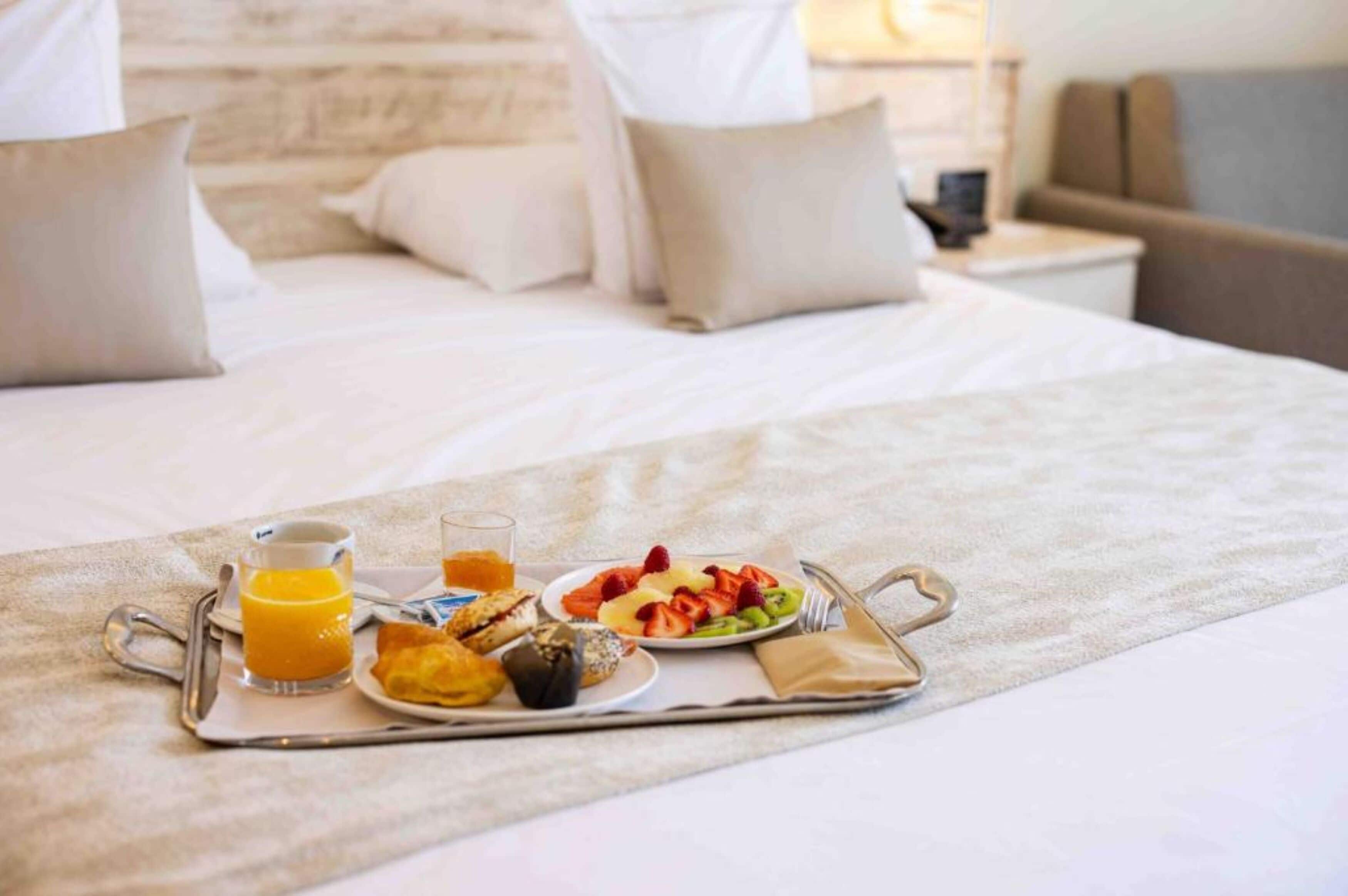 Een net opgemaakt bed met een ontbijtplateau, inclusief toast, fruit en sap.