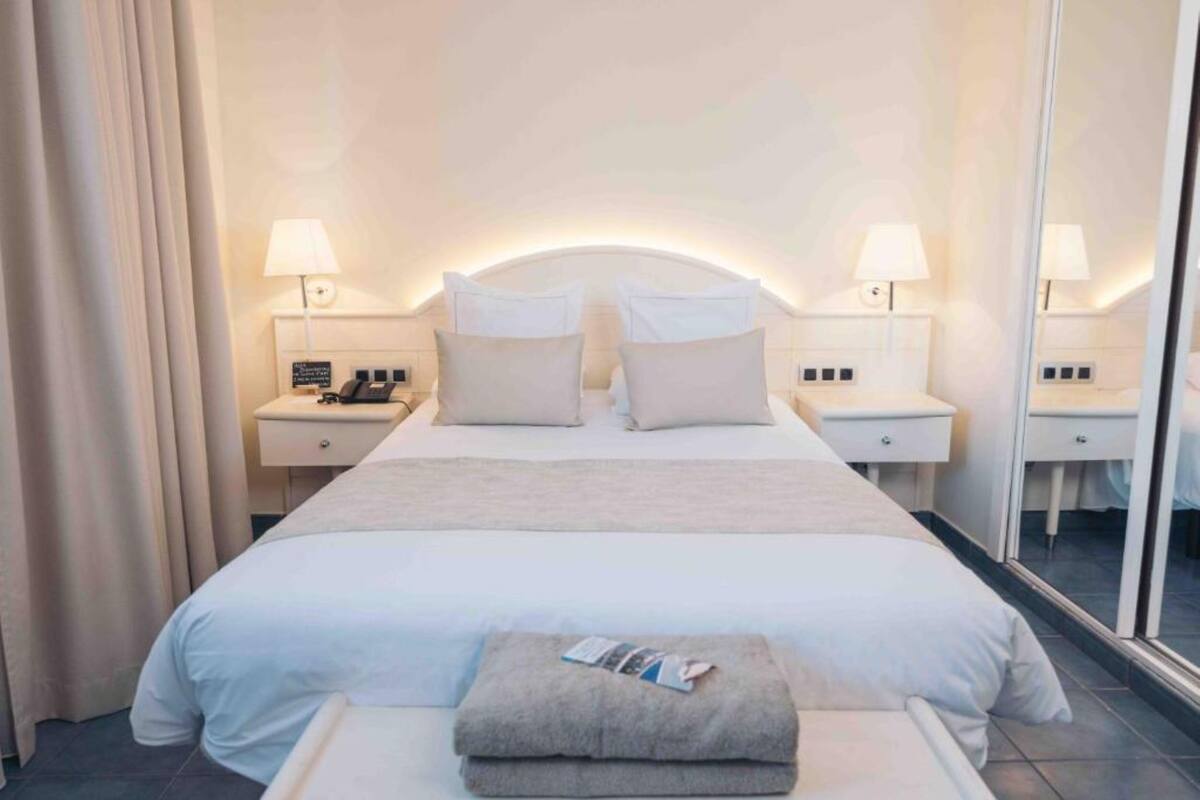 A hotel room with a large bed, two bedside tables with lamps, a mirror, and a window.