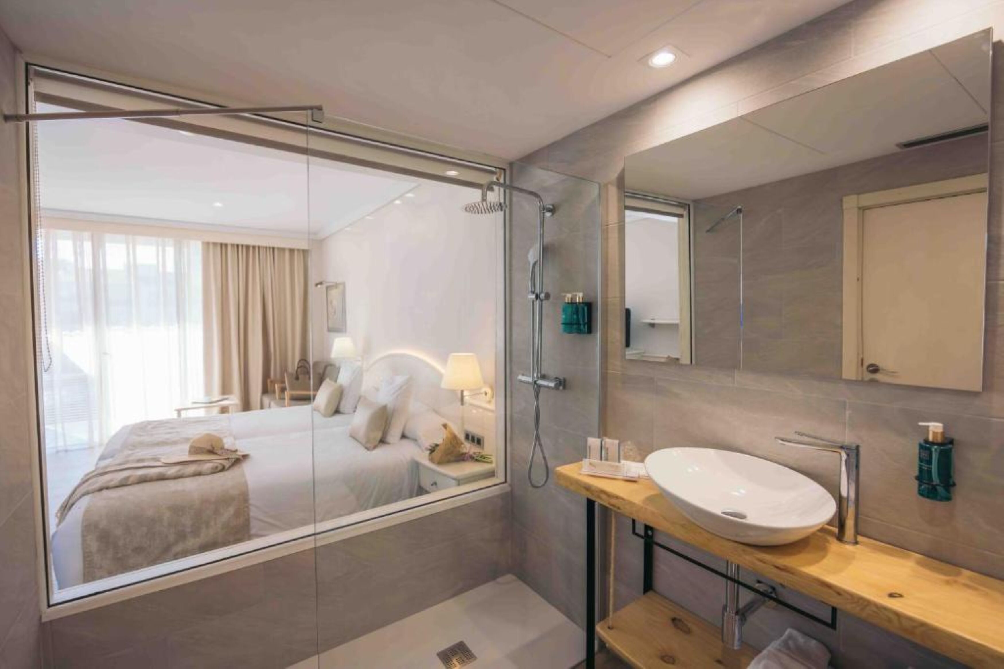 A modern hotel bathroom with a glass-enclosed shower, a large mirror, and a wooden vanity.
