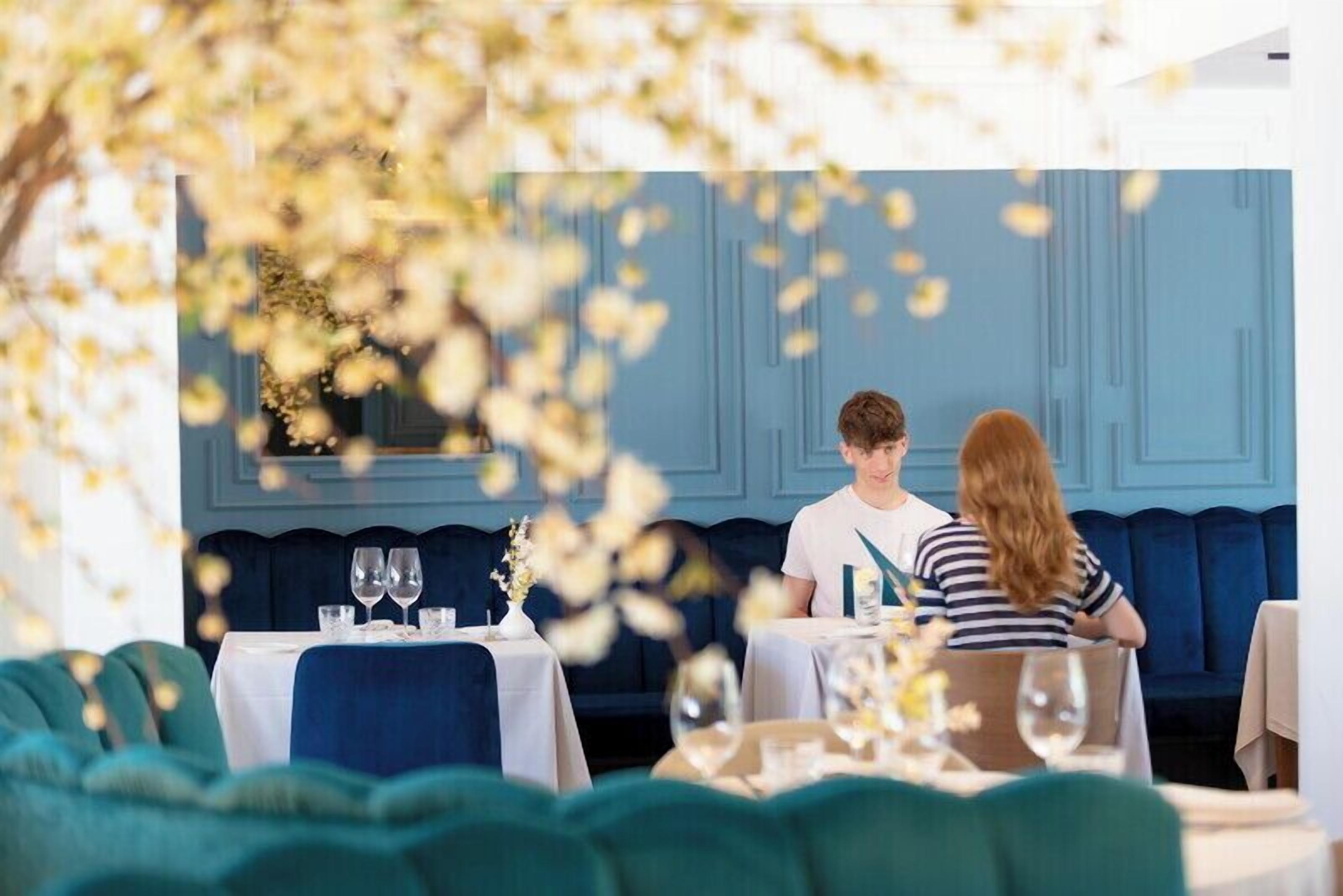 A restaurant with a blue interior, tables set with white tablecloths, and a blue sofa in the background.