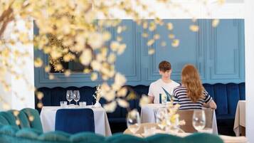 A restaurant with a blue interior, tables set with white tablecloths, and a blue sofa in the background.