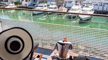 Un balcon donnant sur une marina, une chaise, une table et une bouteille.