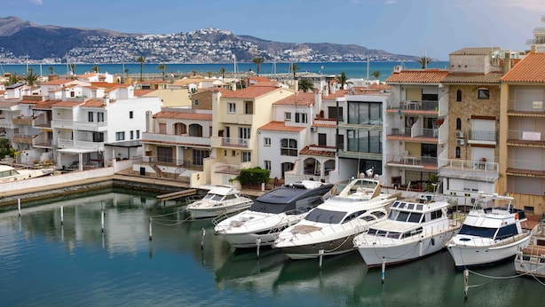 A marina with several boats docked, surrounded by residential buildings with balconies and terraces. - Hotel Port Salins by Pierre & Vacances (Castello d'Empuries)