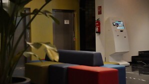 Un hall d’entrée avec un canapé, un extincteur et un kiosque d’information numérique.