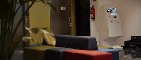 A lobby with a sofa, a fire extinguisher, and a digital information kiosk.