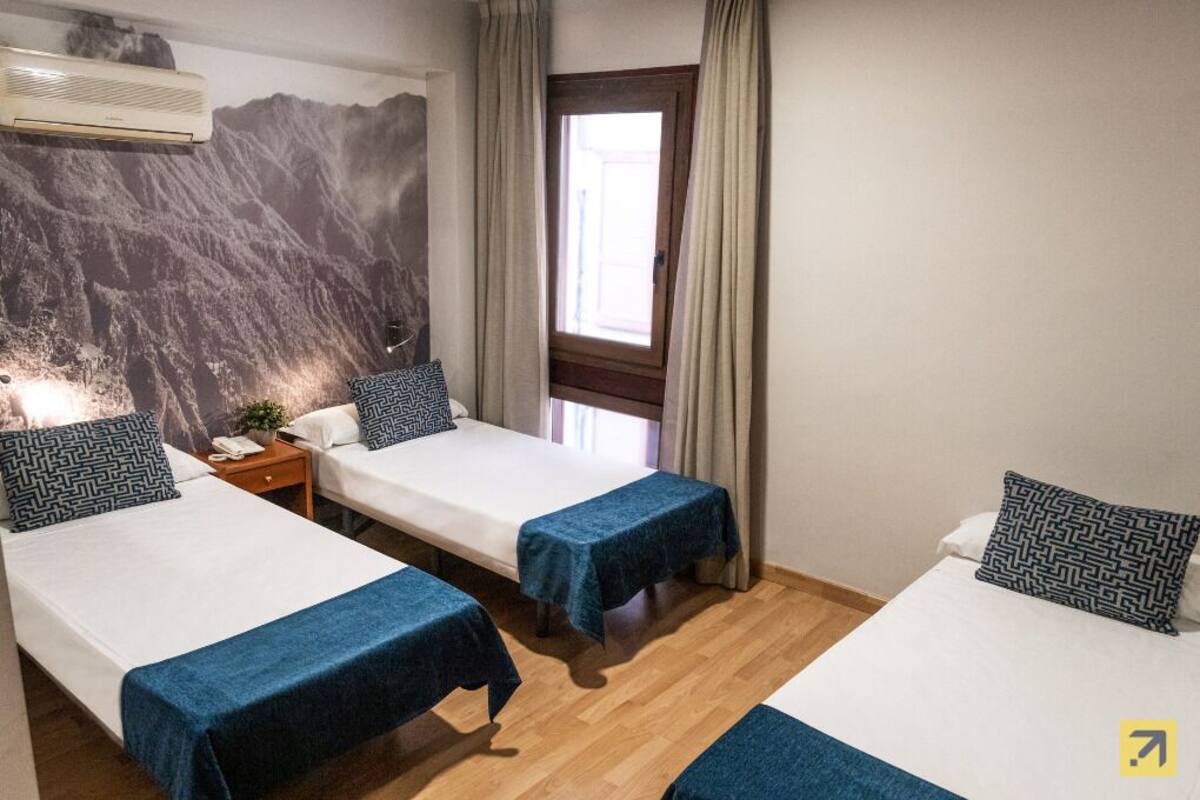 Ein Hotelzimmer mit zwei Einzelbetten, einem hölzernen Nachttisch, einer Wand-Klimaanlage und einem Fenster mit Vorhängen.