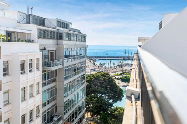 A high-rise building with multiple balconies overlooking a marina and the sea.
