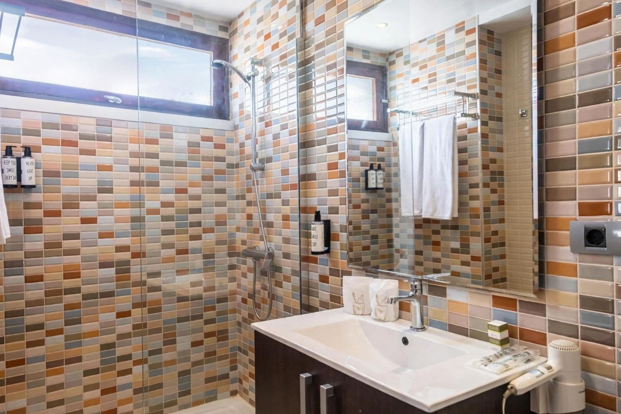 A bathroom with a tiled shower, a sink with a mirror, and a window above the sink.
