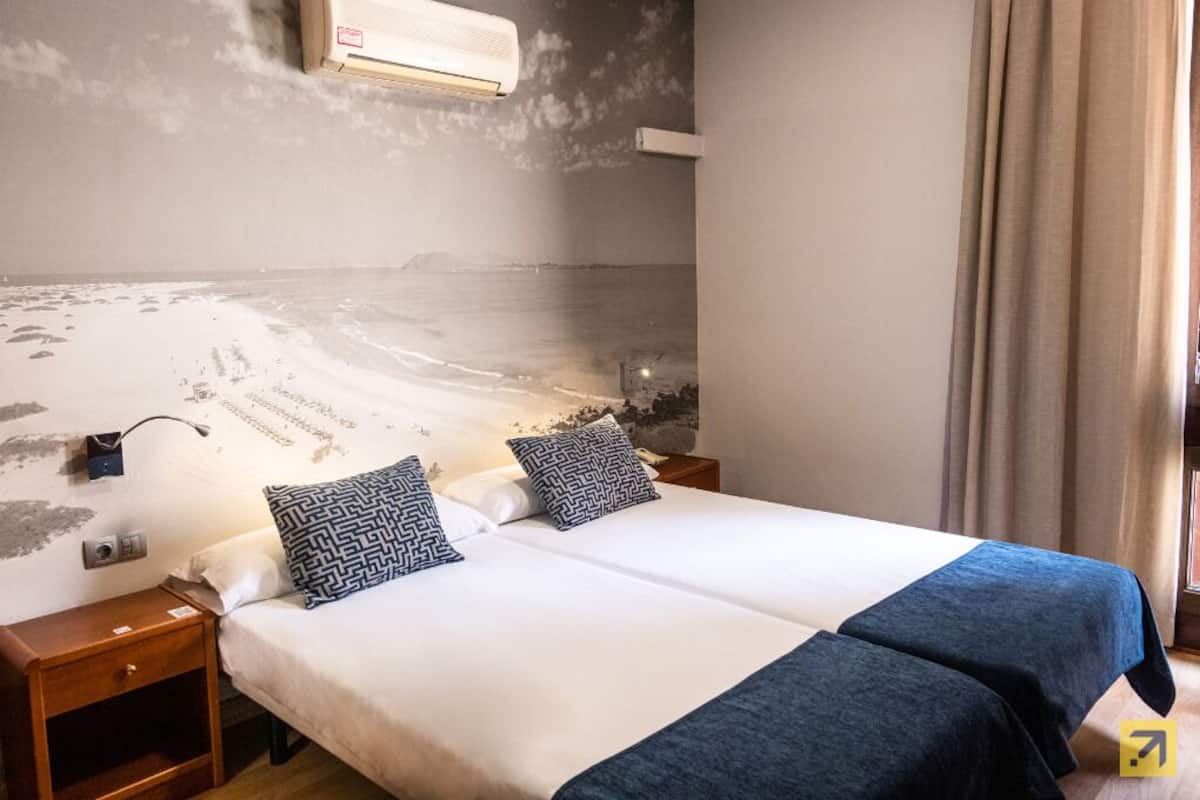 Ein Doppelbett mit gemusterten Kissen, ein Nachttisch und eine wandmontierte Klimaanlage.