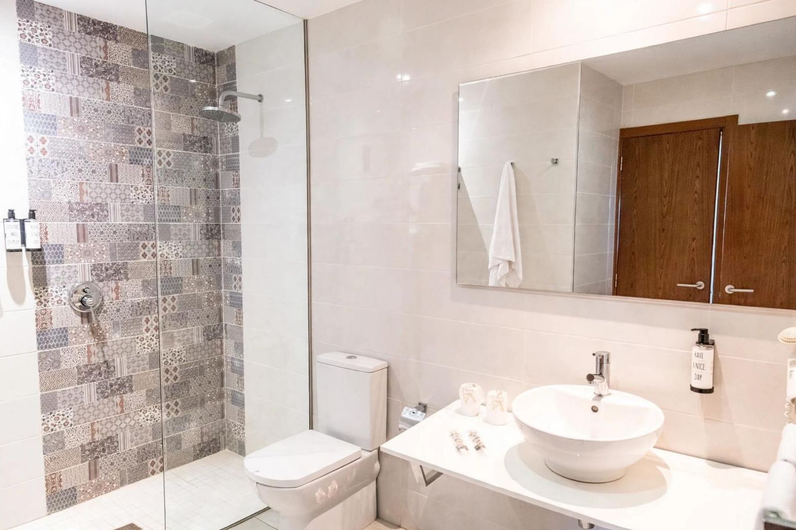 Ein modernes Badezimmer mit Duschkabine aus Glas, einer weißen Toilette, einem großen Spiegel und einem weißen Waschbecken mit runder Schüssel.