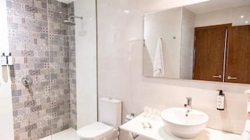 Ein modernes Badezimmer mit Duschkabine aus Glas, einer weißen Toilette, einem großen Spiegel und einem weißen Waschbecken mit runder Schüssel.