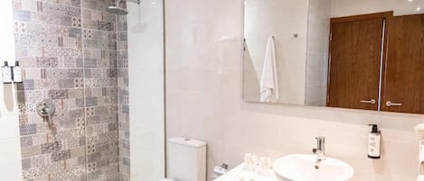 A modern bathroom with a glass shower enclosure, a white toilet, a large mirror, and a white sink with a round basin.