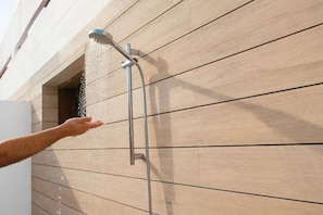 Une main tendue vers un pommeau de douche fixé au mur, dont l’eau jaillit.