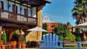 A courtyard with outdoor seating, a white Adirondack chair, and a stone building with a balcony. - Palación de Toñanes (Alfoz de Lloredo)
