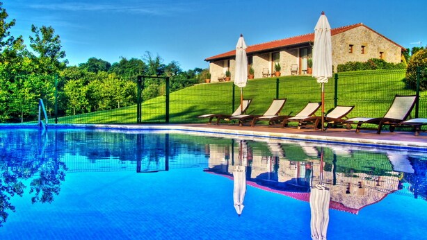 A swimming pool with lounge chairs and umbrellas, surrounded by a fence and greenery. - Palación de Toñanes (Alfoz de Lloredo)
