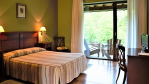 A hotel room with a bed, two bedside lamps, a desk with a chair, and a view of the outdoors through a sliding door. - Palación de Toñanes (Alfoz de Lloredo)
