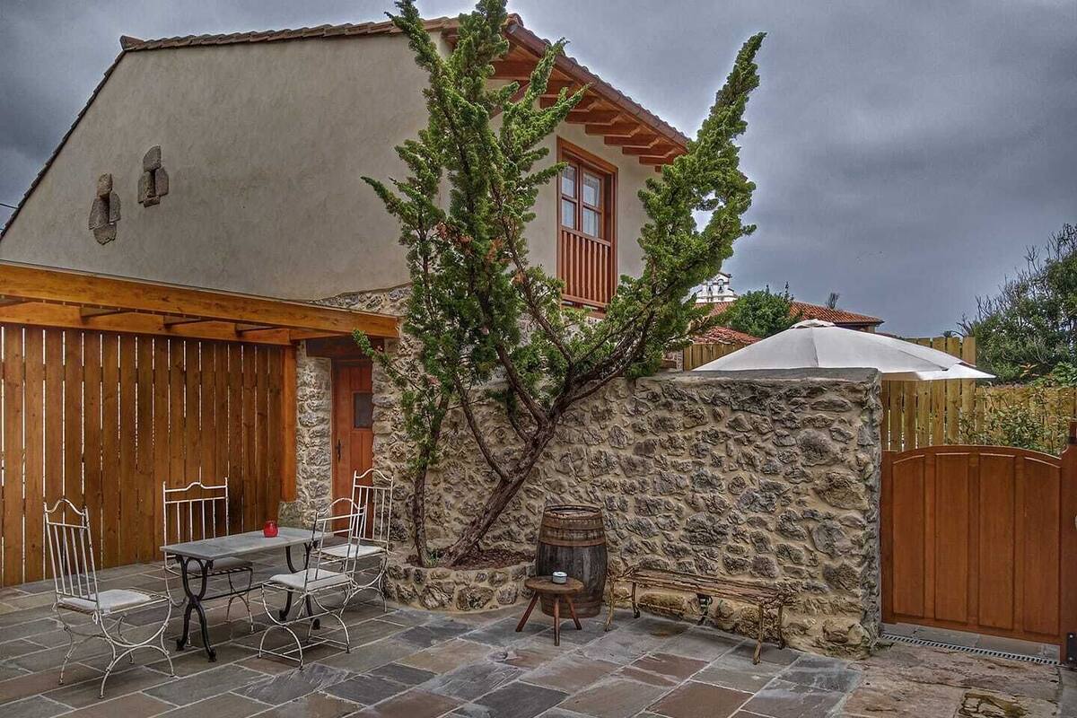A stone patio with a table and chairs, a wooden door, and a stone wall with a tree.