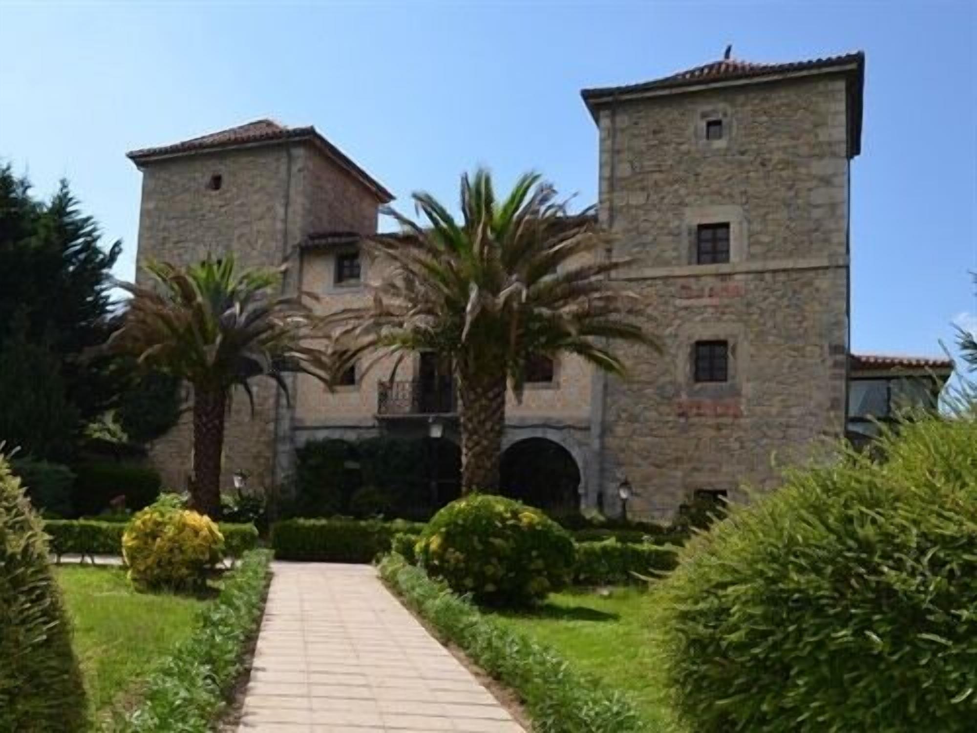 A stone building with a central courtyard, palm trees, and a paved walkway.